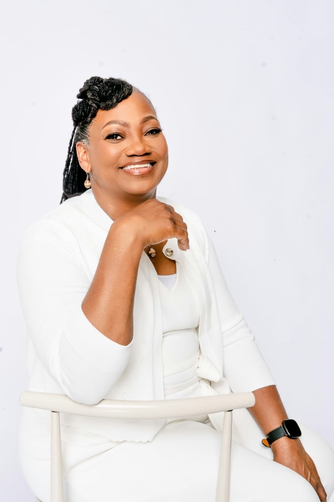 A smiling woman in white resting her chin on her hand.